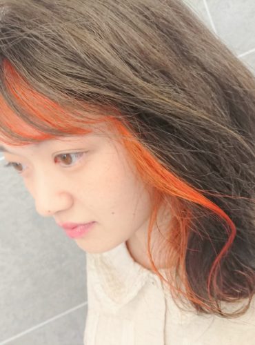 肩にかかる長さの顔周りの髪色が橙色のヘアスタイル