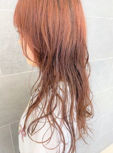 肩甲骨が隠れる程の長さの赤橙色のヘアスタイル