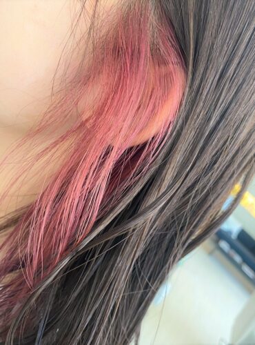 イヤリングみたいにピンクのヘアカラーを顔周りにだけしている女性の横顔